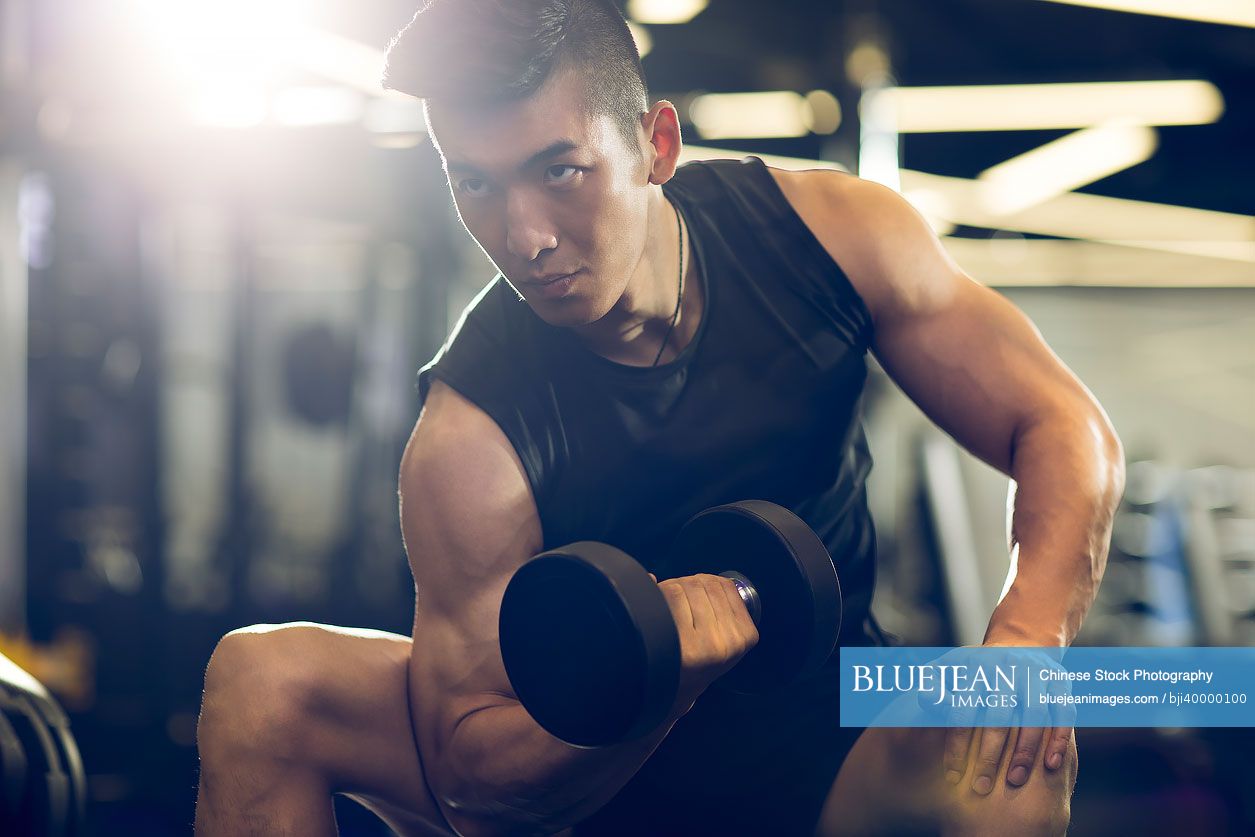 Young Chinese man working out with dumbbell at gym