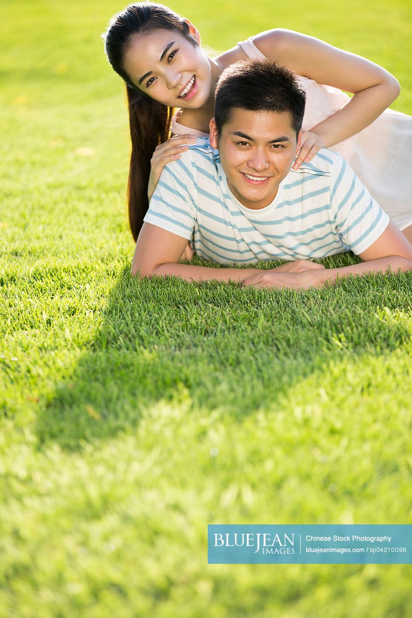 Cheerful young Chinese couple lying down on grass