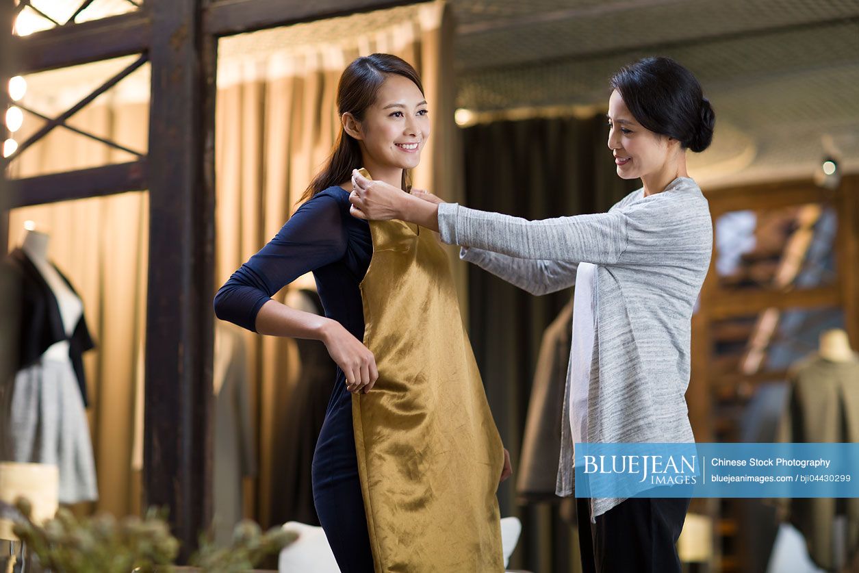 Chinese clothing store owner helping customer with choosing dress