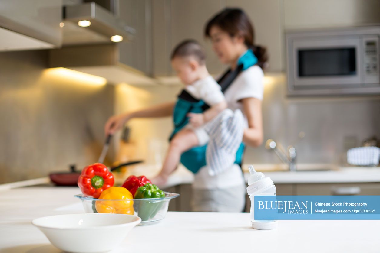 Chinese mother holding baby and cooking in the kitchen