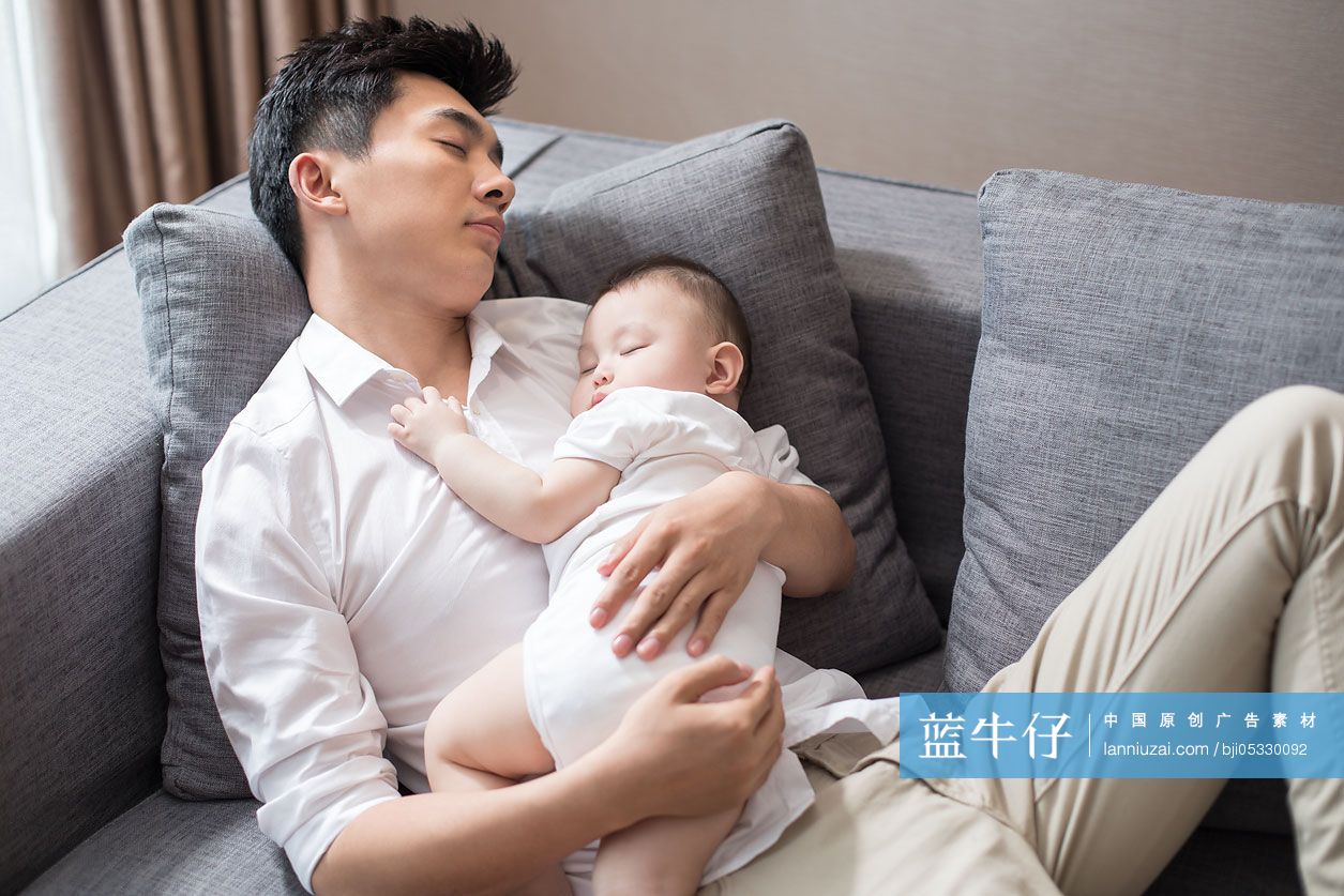 年轻爸爸抱着宝宝在沙发上睡觉