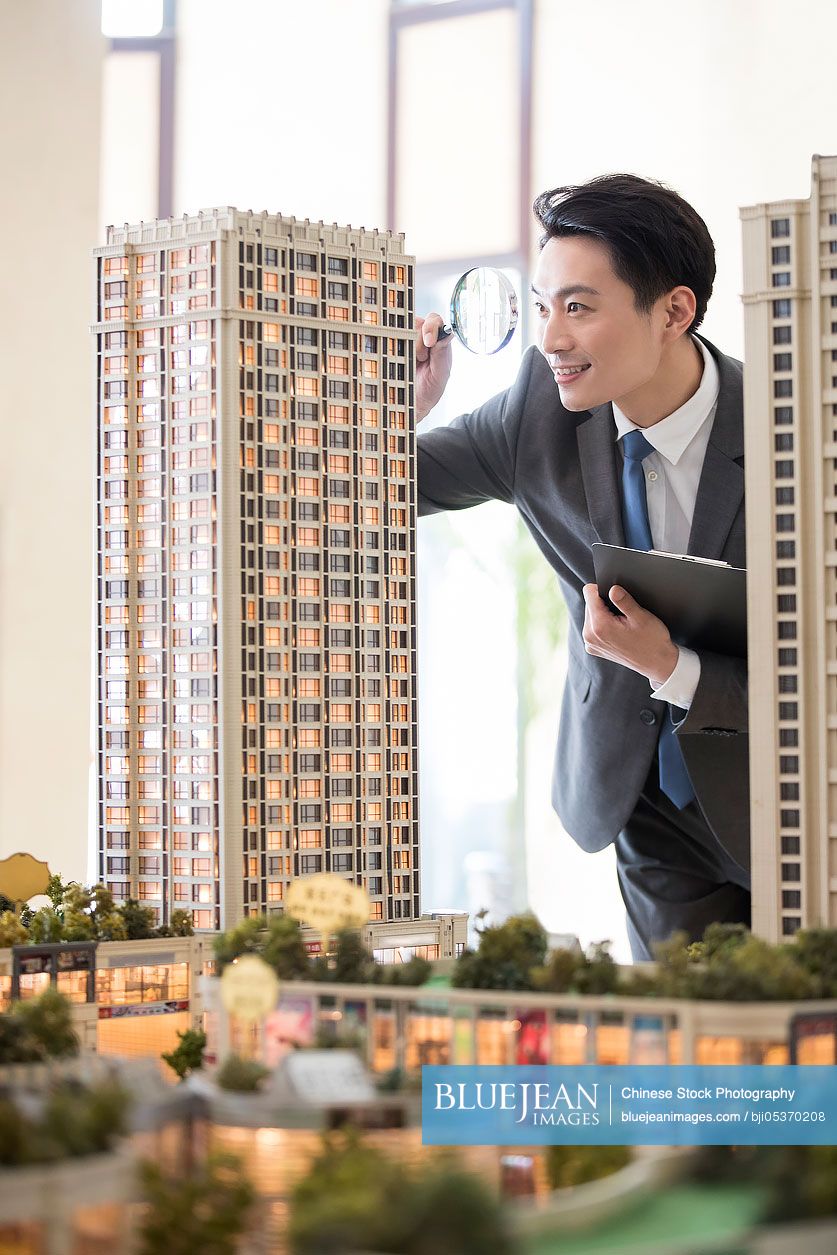 Chinese realtor checking architectural model through magnifying glass