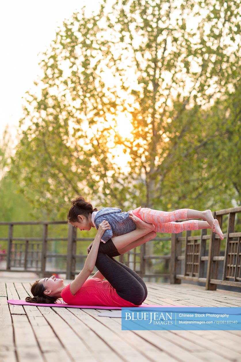Happy Chinese mother and daughter doing yoga outdoors