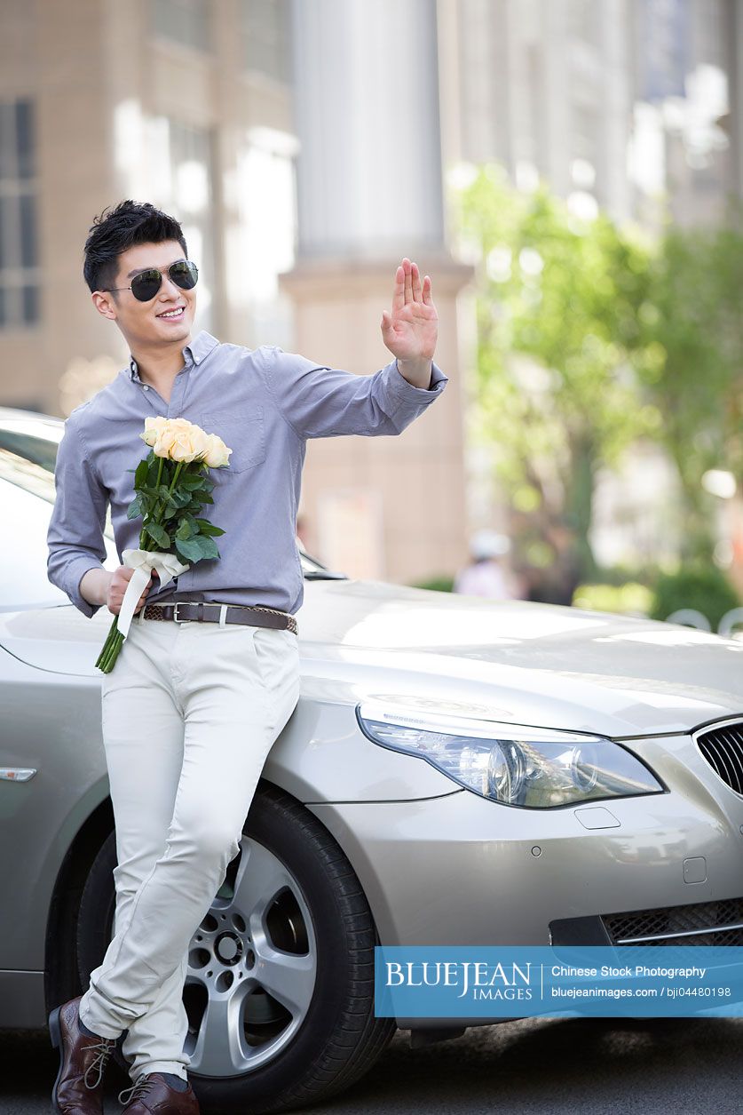 Young Chinese man leaning against his car with a bunch of flowers