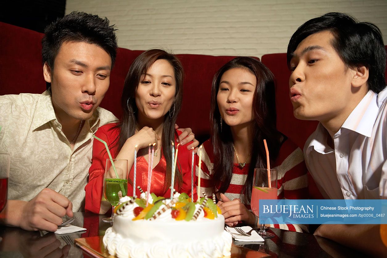 Group of young Chinese people blowing out candles on birthday cake