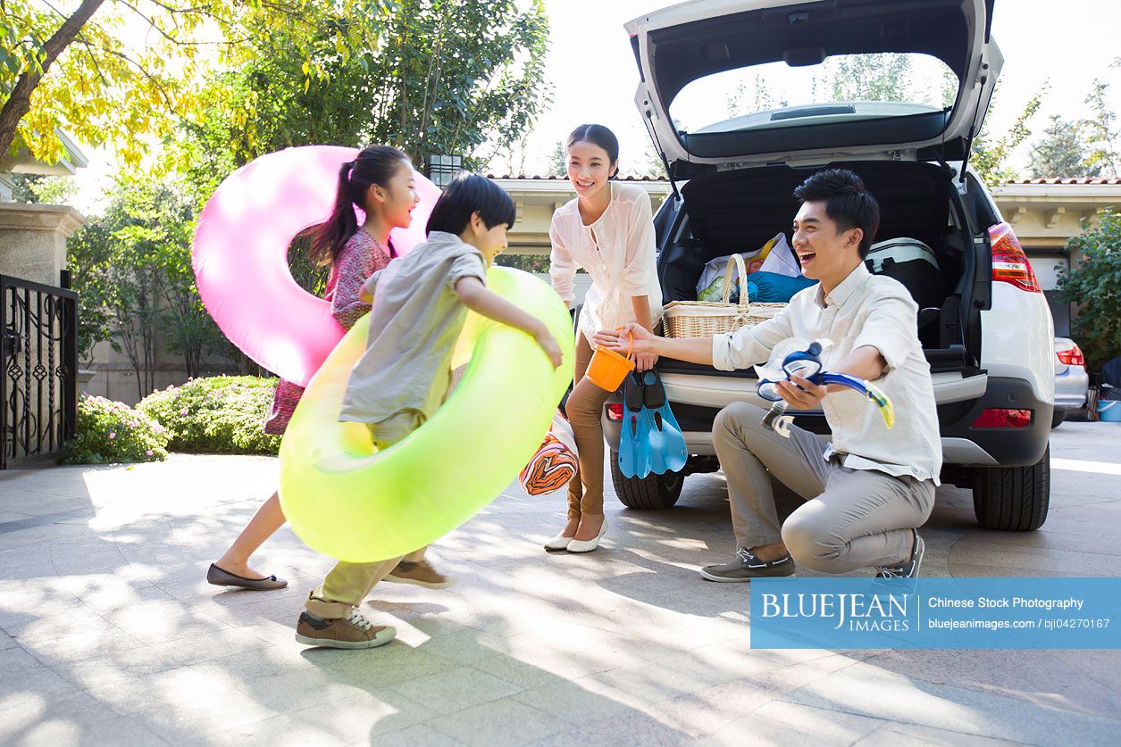 Young Chinese family putting water sports equipment into the car