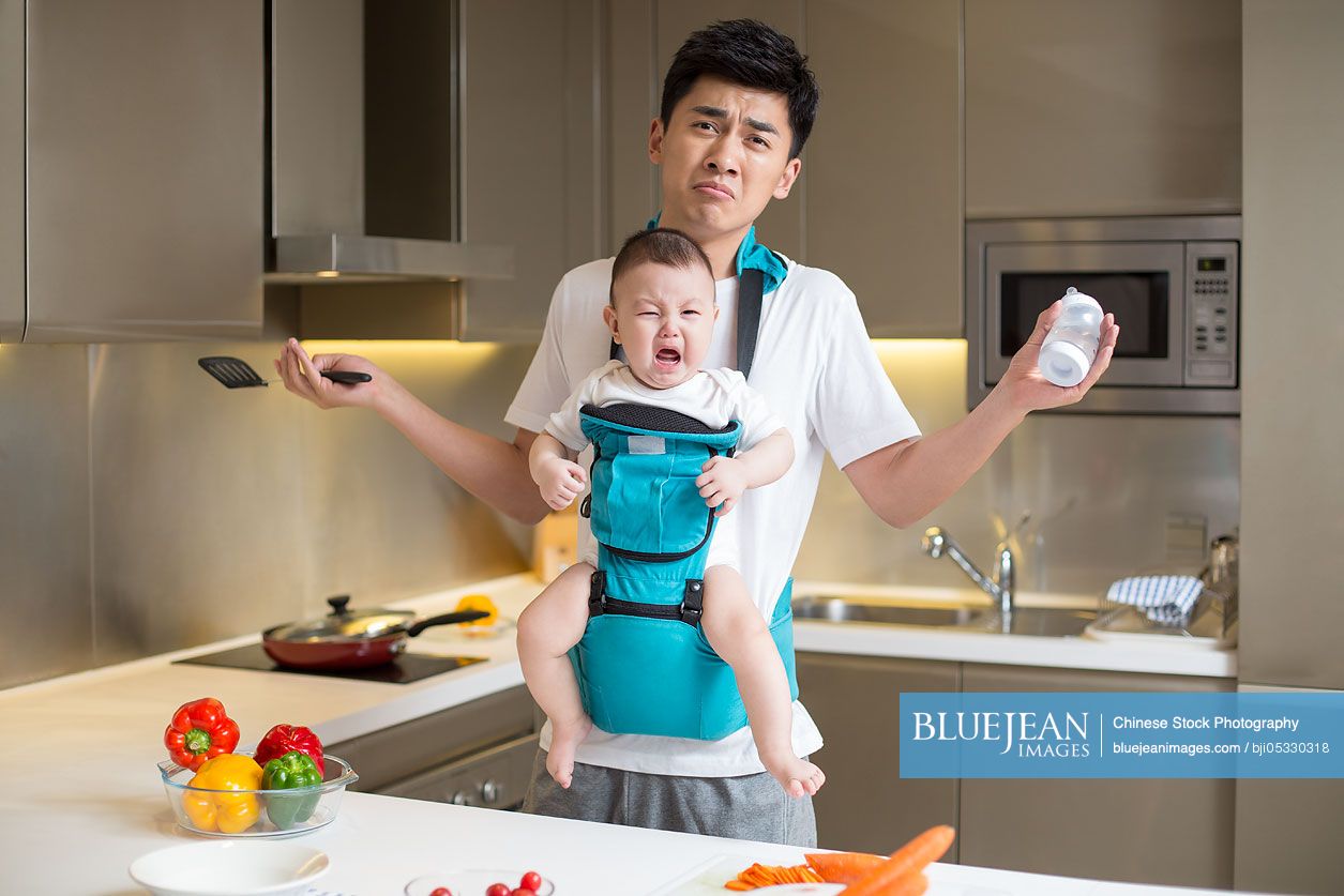 Chinese father holding baby and cooking in the kitchen
