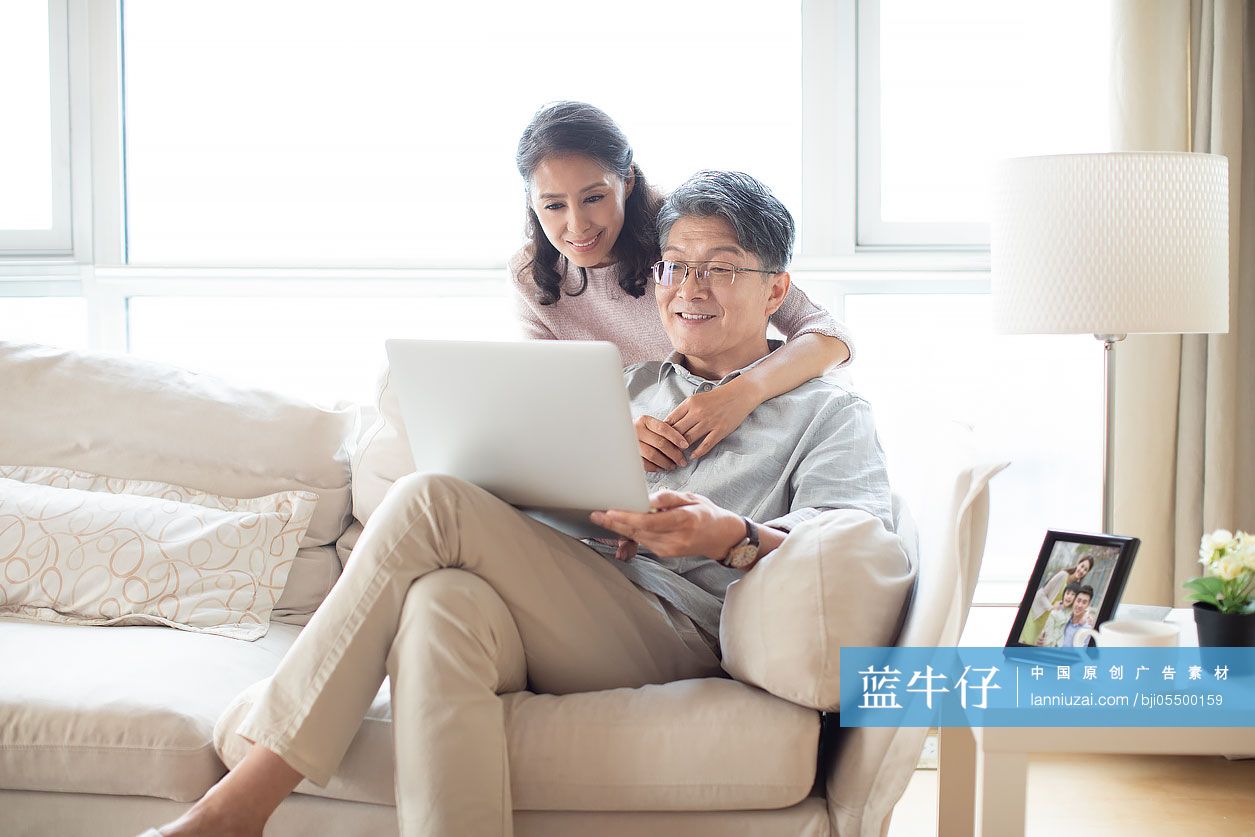 快乐的成熟夫妇在客厅使用笔记本电脑-蓝牛仔影像-中国原创广告影像素材