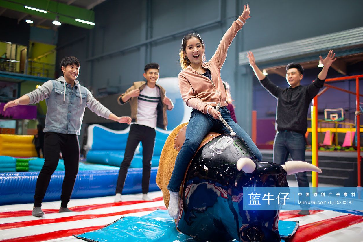 快乐的年轻朋友在游乐场玩电动骑牛机