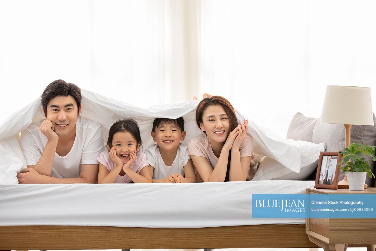 Happy young Chinese family relaxing in bed
