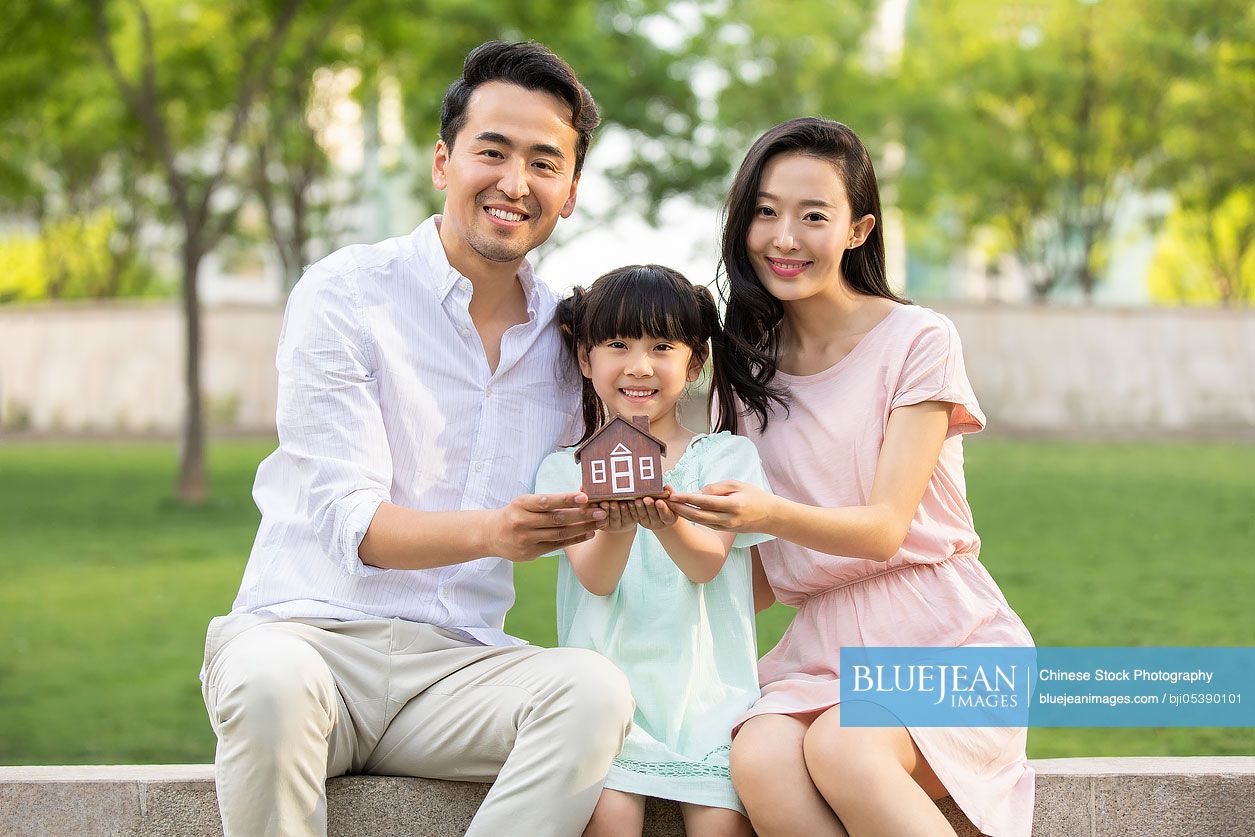 Happy young Chinese family holding a toy house