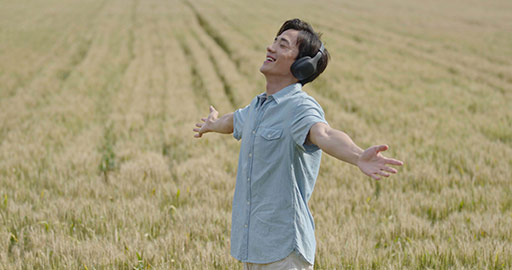 Happy young Chinese man wearing headphones in wheat field,4K