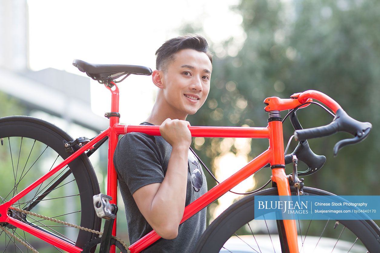 Young Chinese man carrying bicycle on shoulder