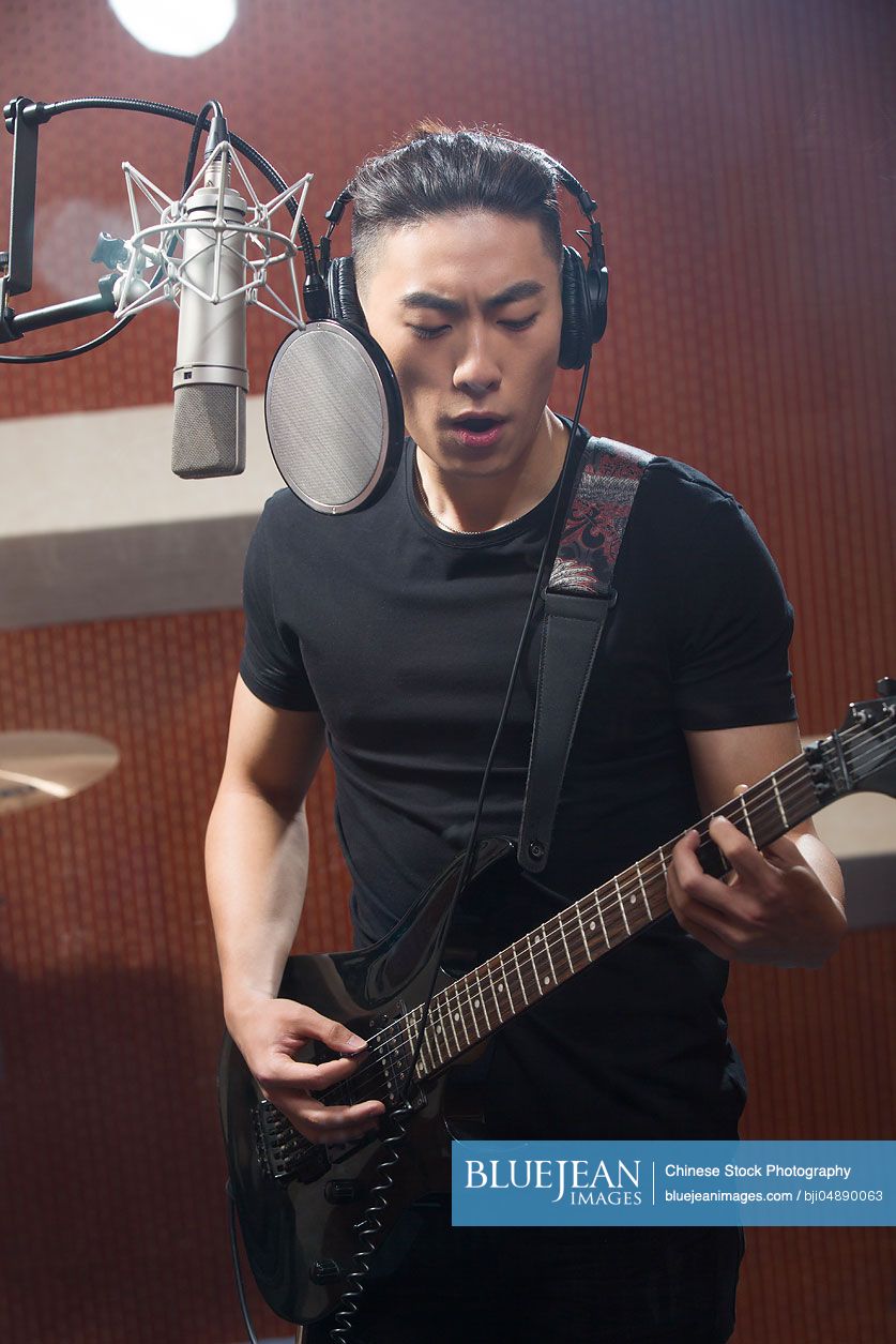 Young Chinese man singing with guitar in recording studio