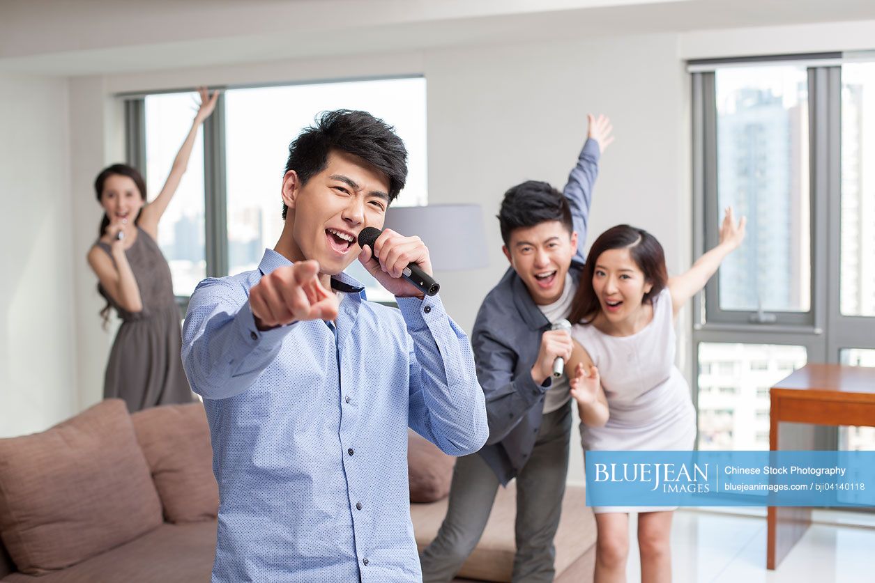 Happy young Chinese friends singing and dancing in living room