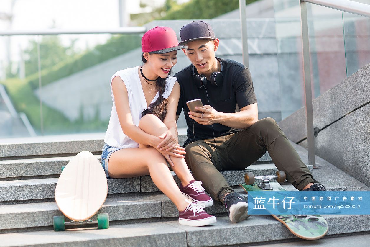 带着滑板的快乐年轻情侣坐在台阶上看手机