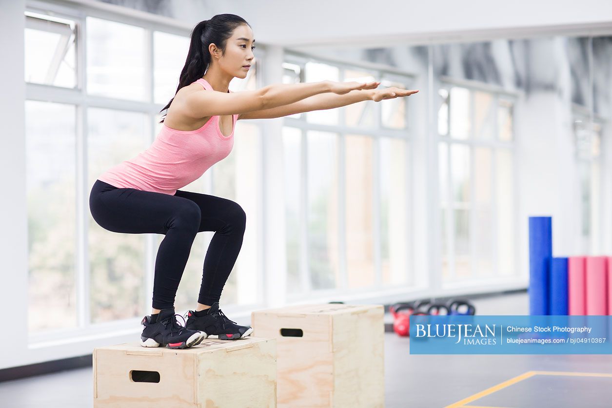 Young Chinese woman doing box jump in crossfit gym