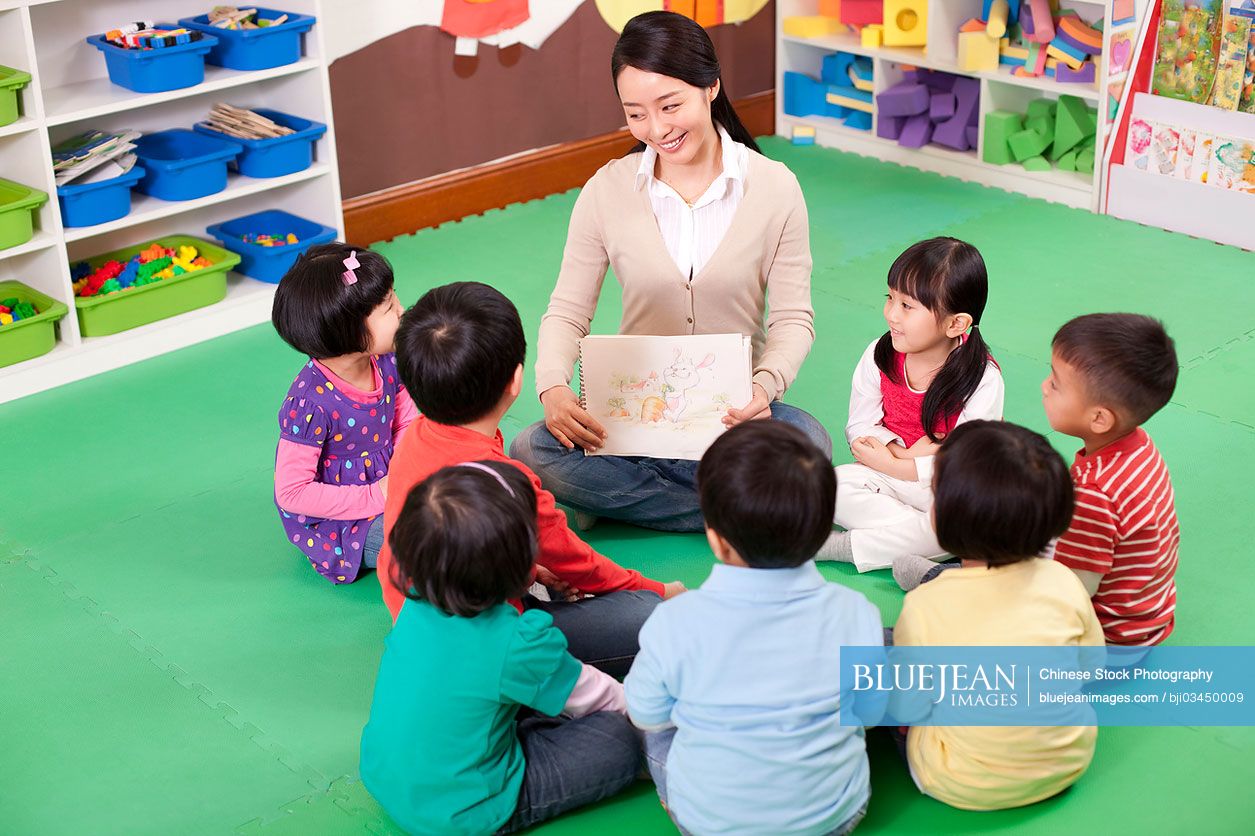 Female Chinese teacher and cute kindergarten children sitting in a circle