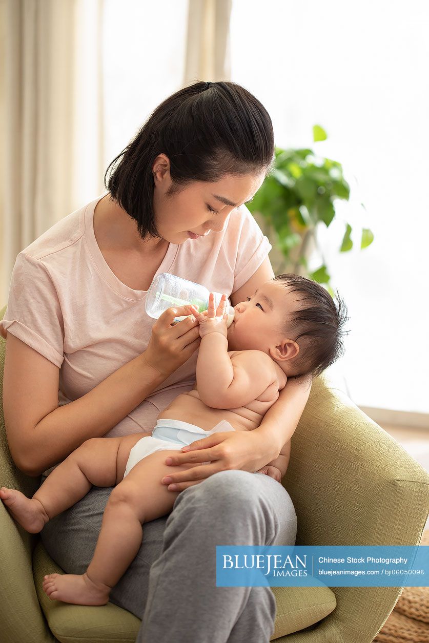 Young Chinese mom feeding baby girl with bottle