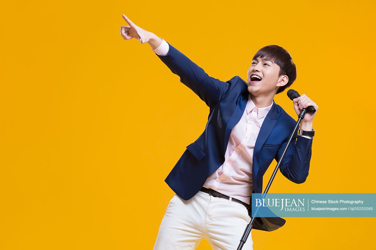 Cheerful young Chinese man singing with microphone