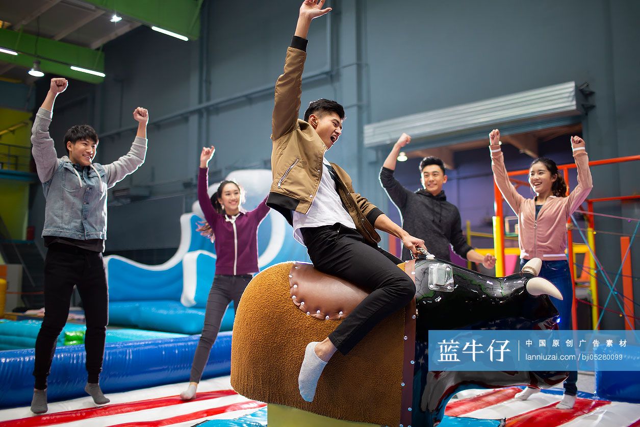 快乐的年轻朋友在游乐场玩电动骑牛机