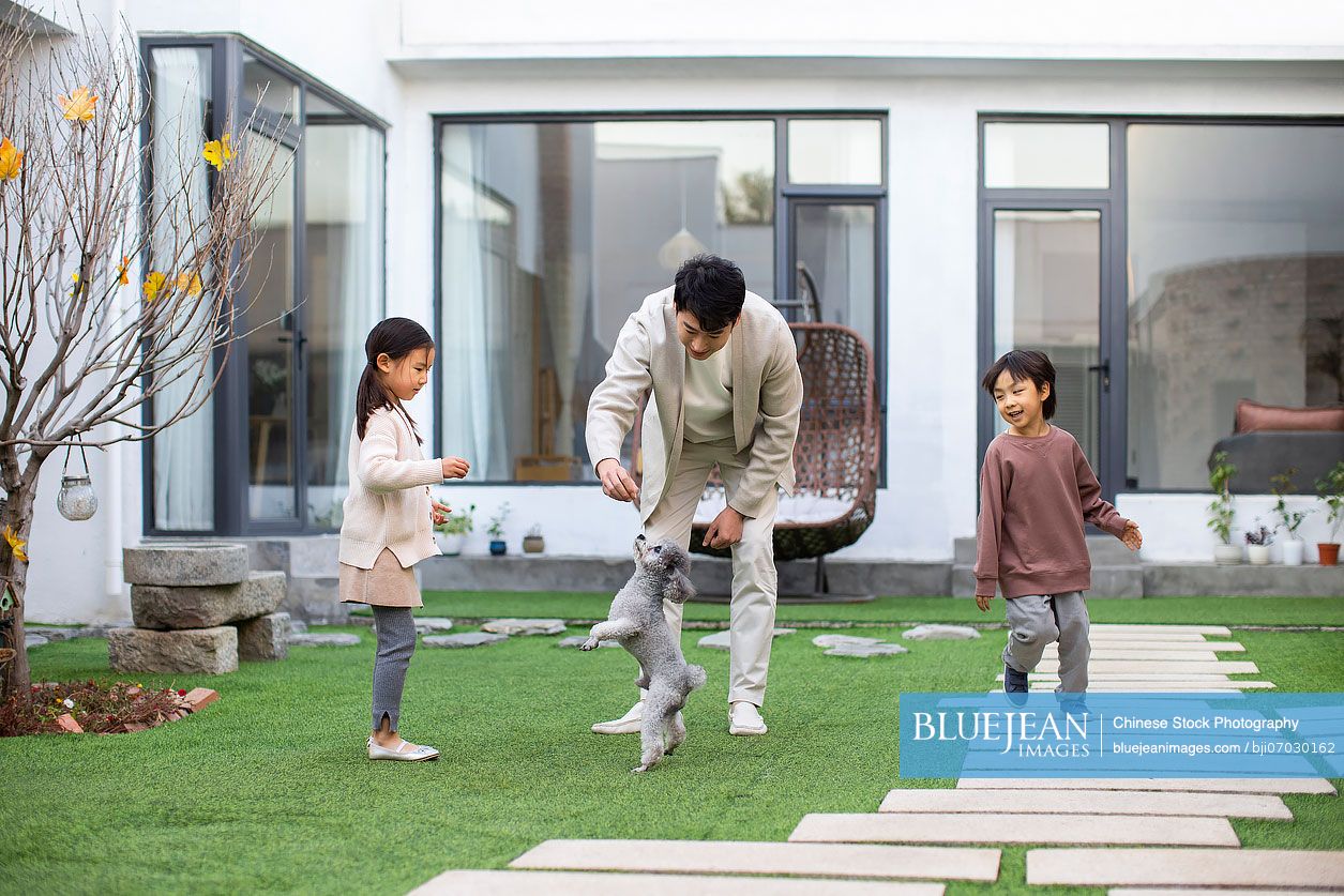 Happy young Chinese family playing with pet dog in the courtyard