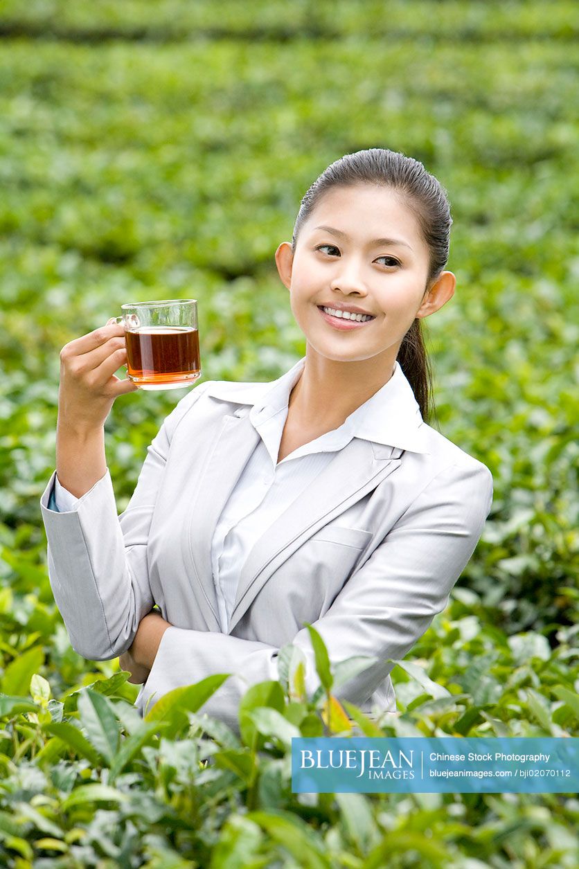 Young Chinese businesswoman in tea field with freshly brewed tea