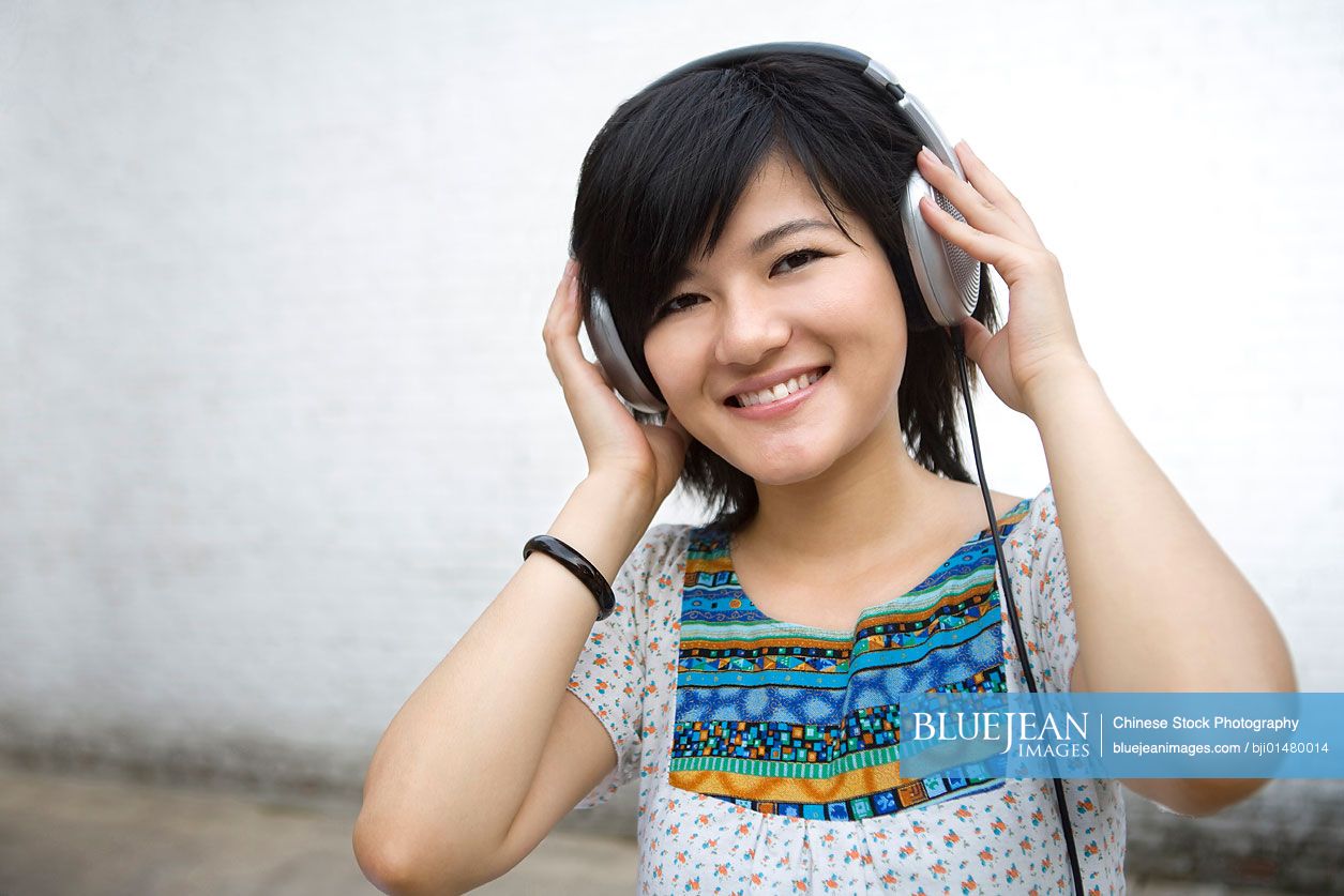 Smiling young Chinese woman listening to music on headphones