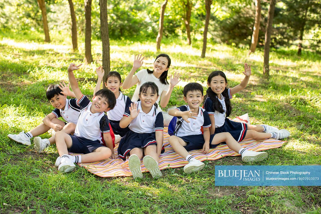 Cheerful Chinese school children picnicking outdoors with their teacher ...