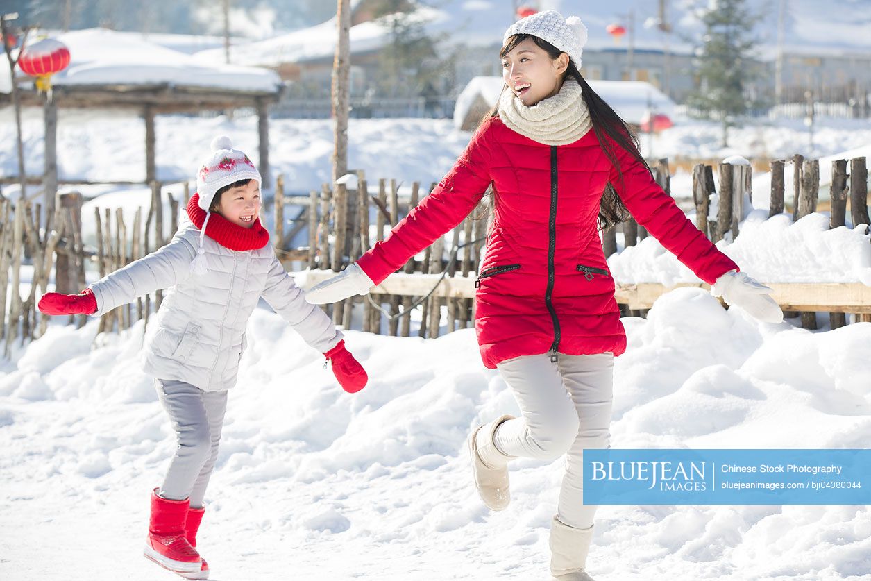 Happy Chinese mother and daughter running in the snow