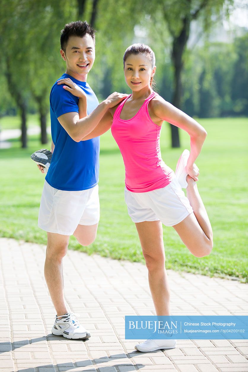 Portrait of young Chinese couple stretching in park