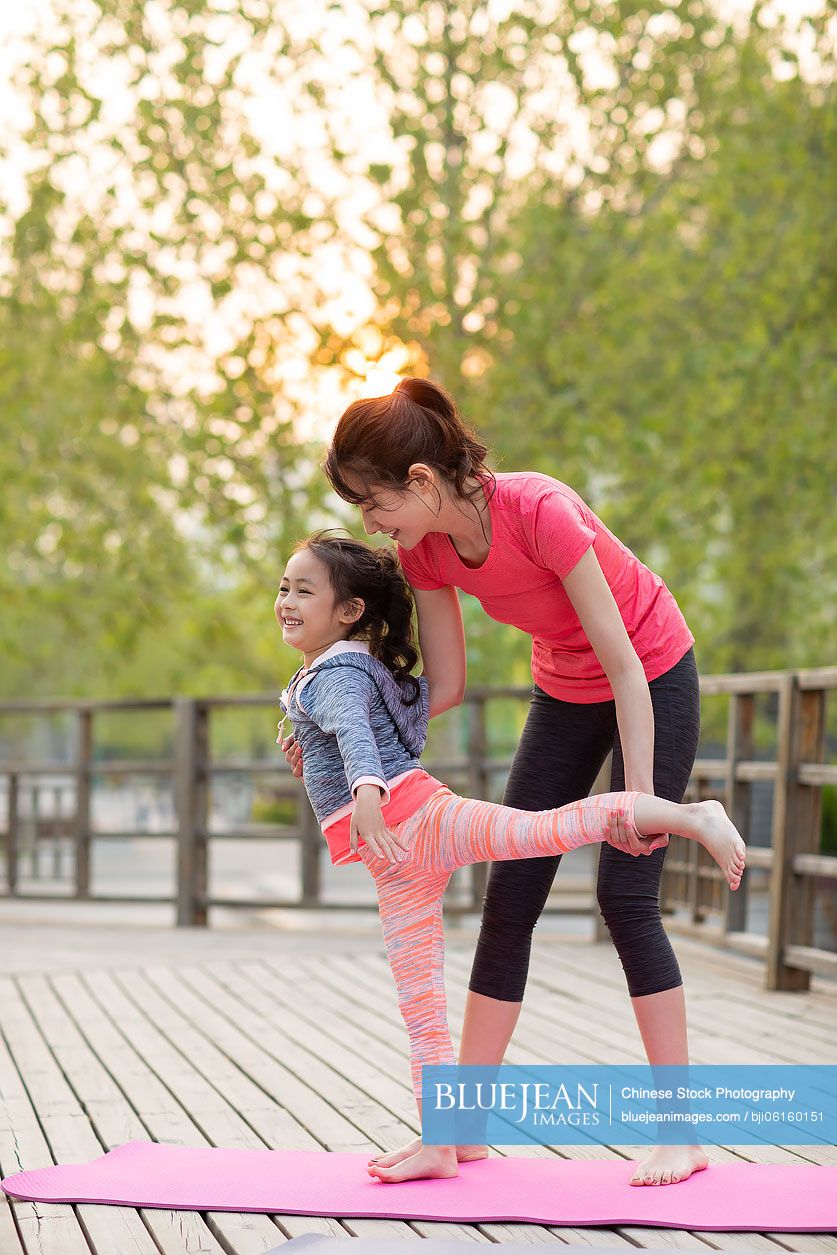 Happy Chinese mother and daughter doing yoga outdoors