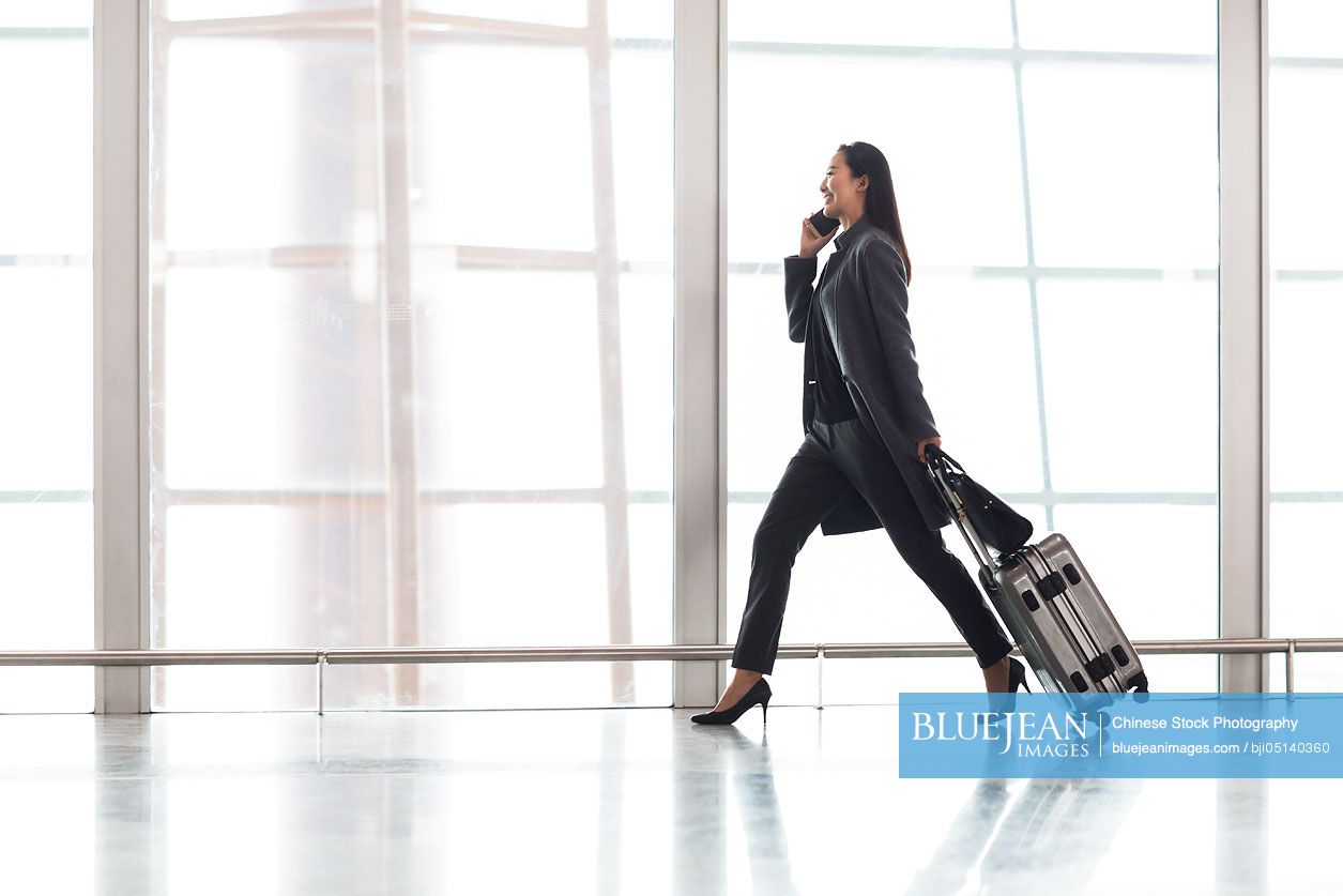Chinese businesswoman pulling wheeled luggage in airport lobby