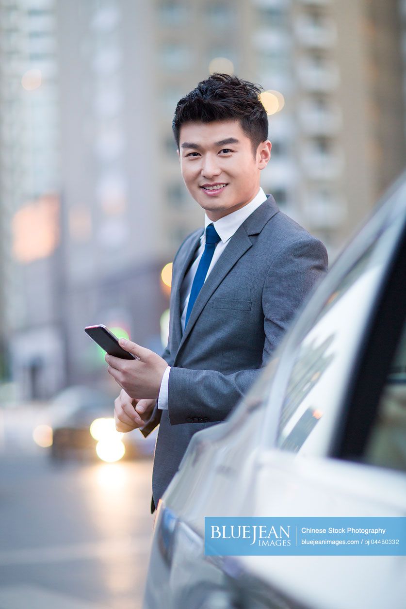 Chinese businessman standing next to the car with smart phone