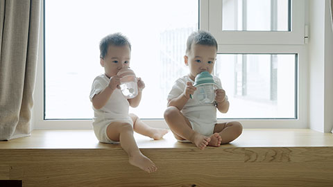 Two twin babies drinking water from their bottles