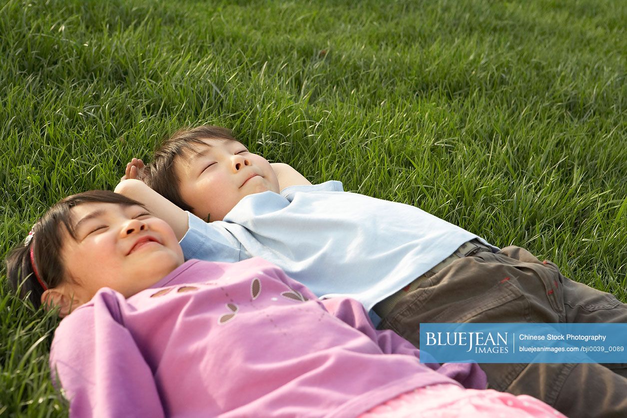 Young Chinese Boy And Girl Laying In The Park Looking At The Sky