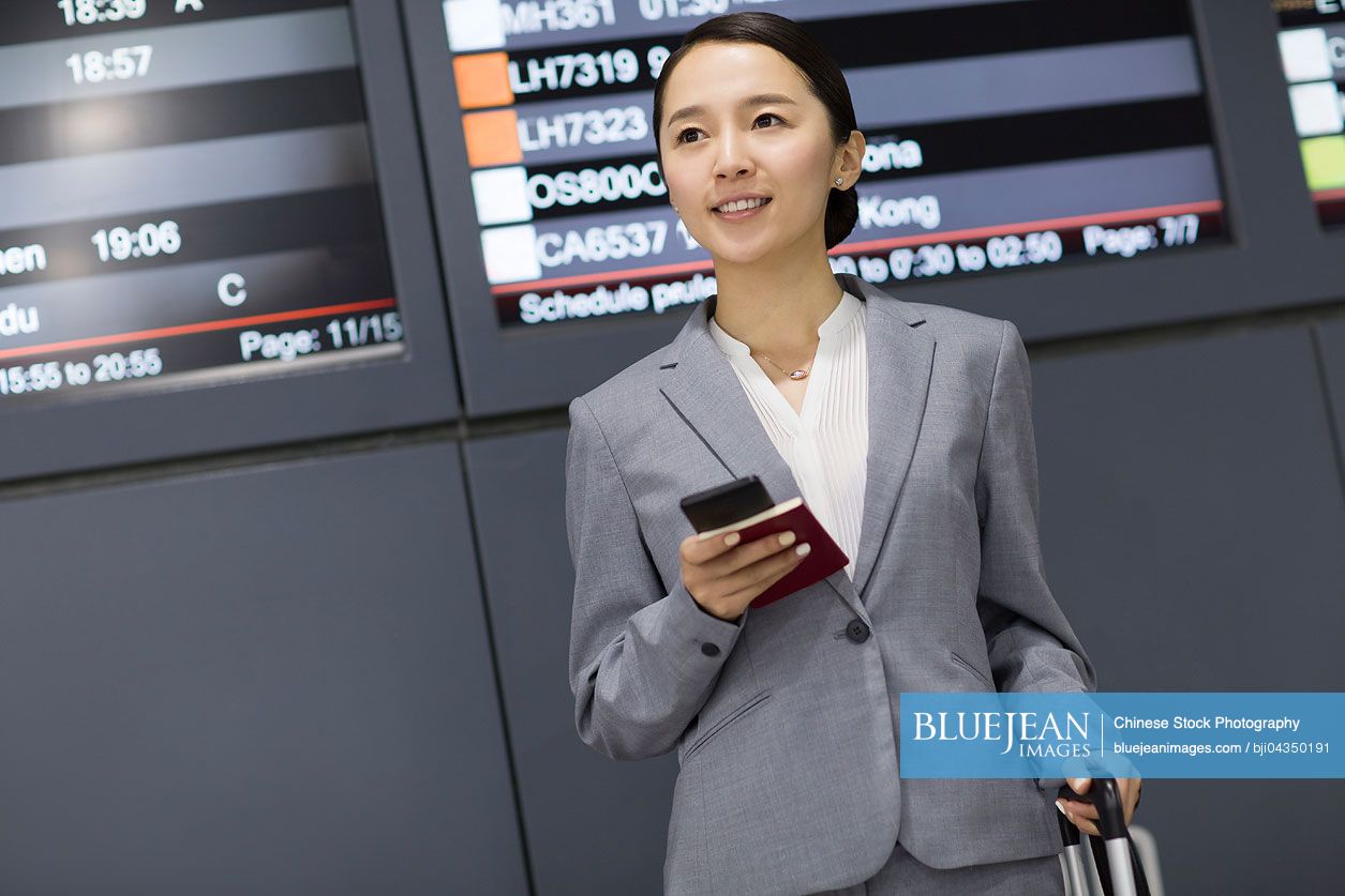 Young Chinese businesswoman holding passport and smart phone in airport