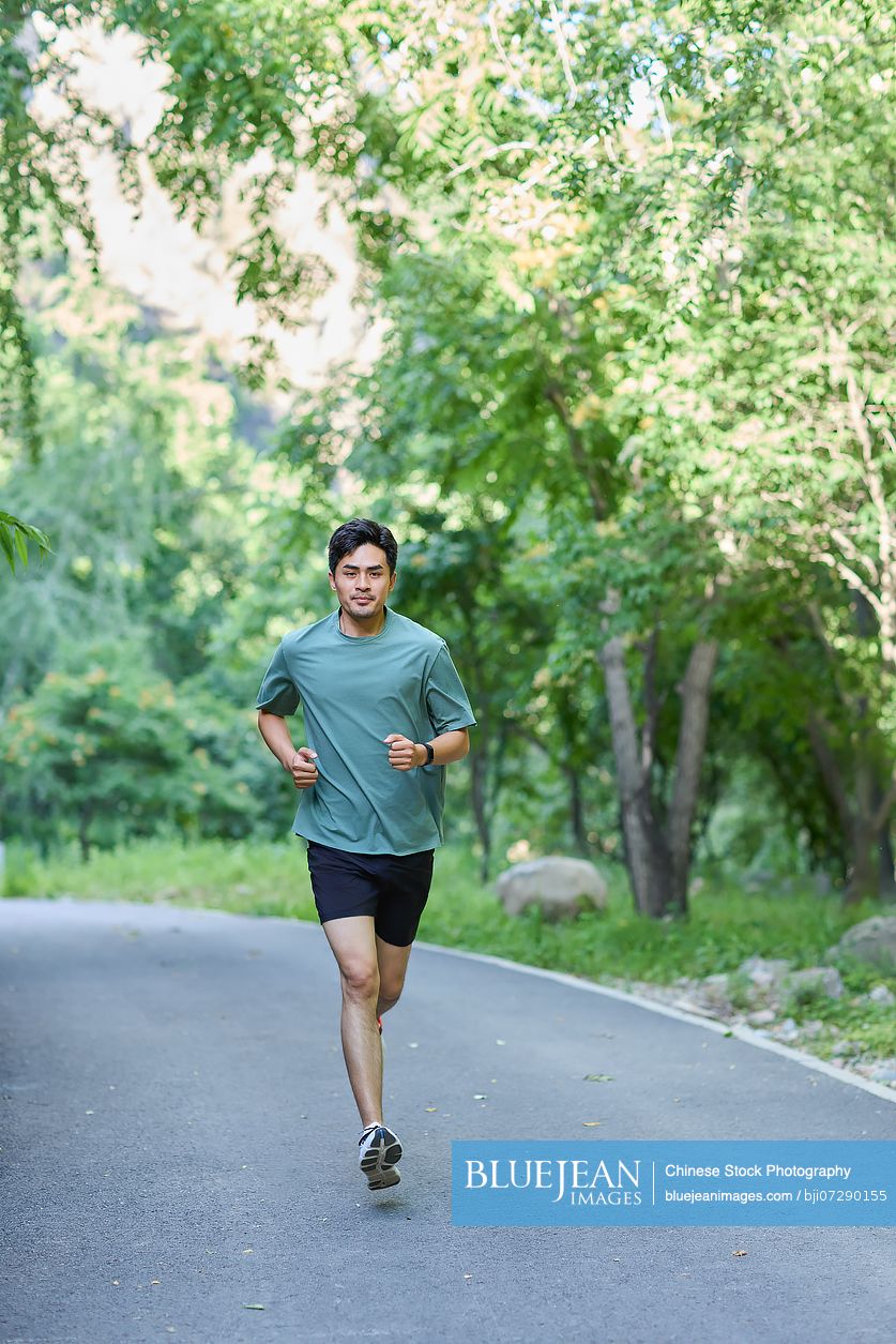 Man jogging along a road surrounded by lush trees