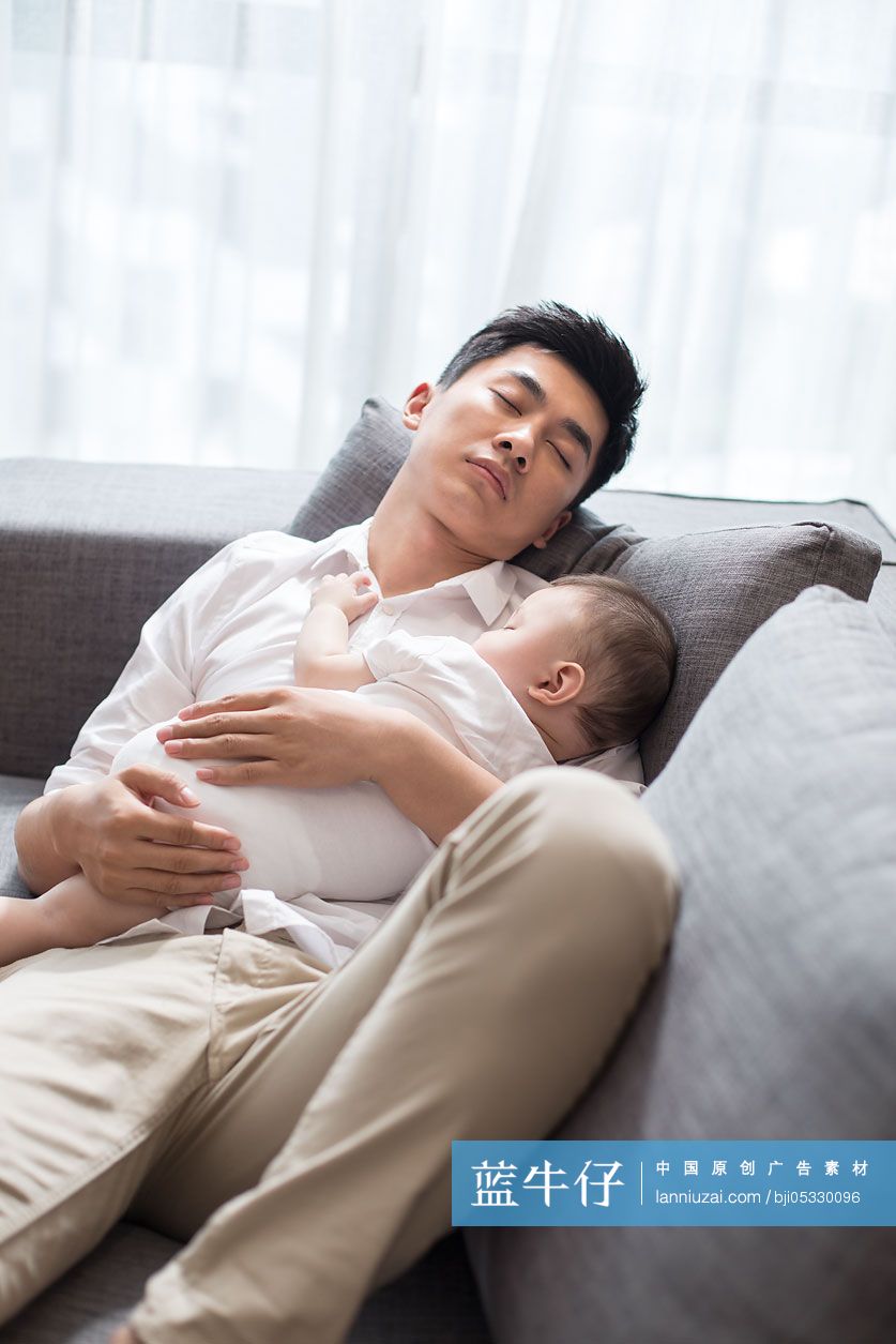 年轻爸爸抱着宝宝在沙发上睡觉