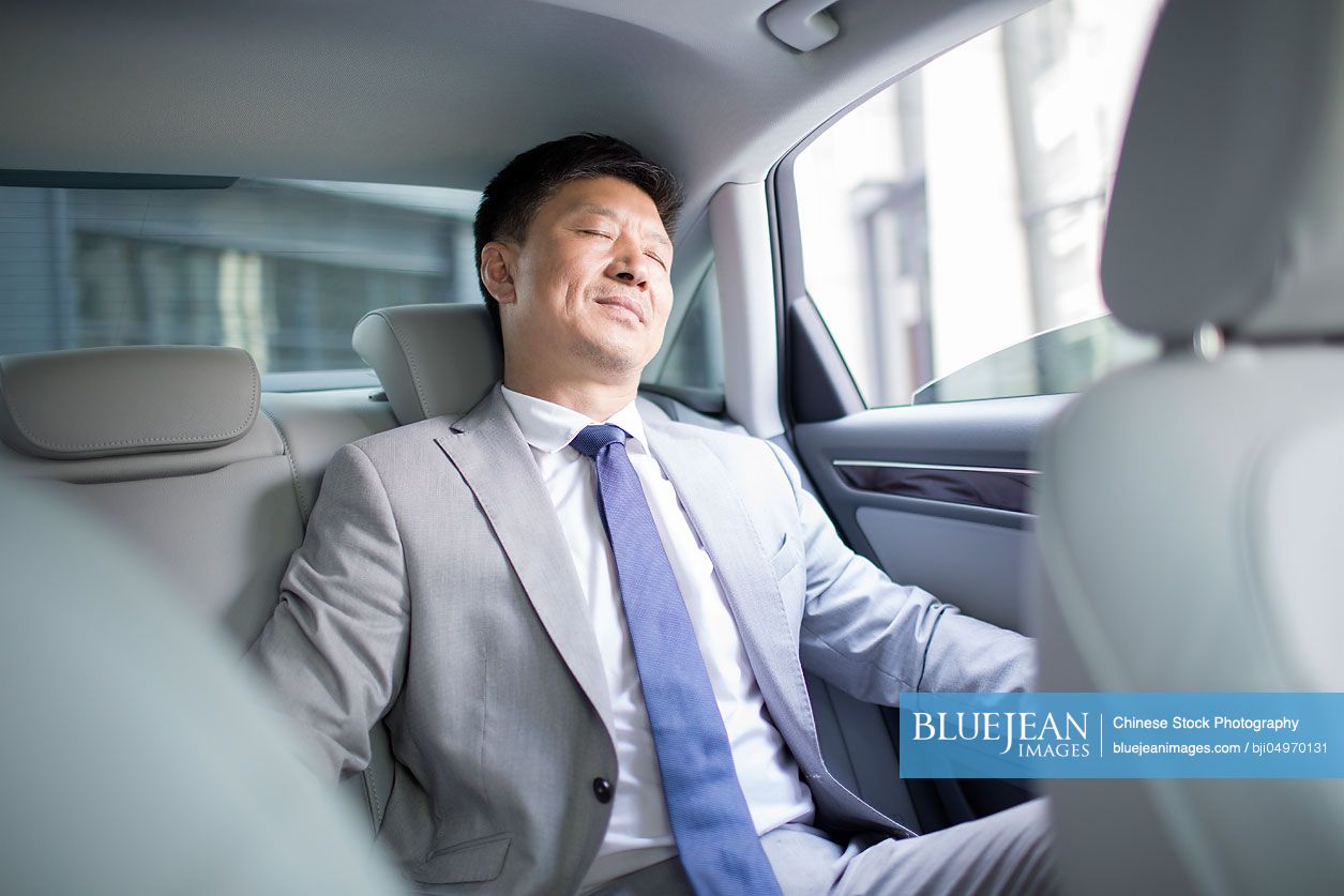 Confident Chinese businessman sitting in car back seat