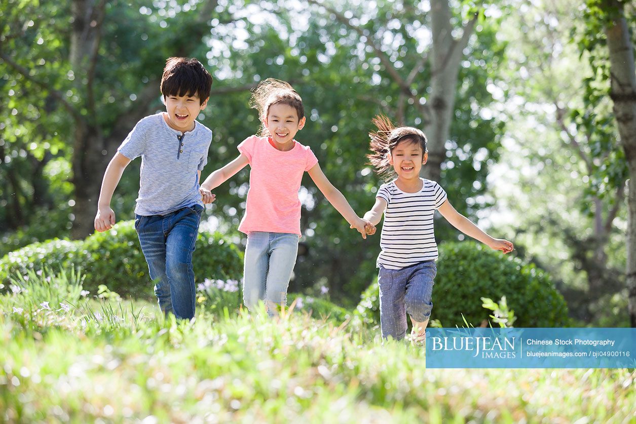 Happy Chinese children holding hands running in woods