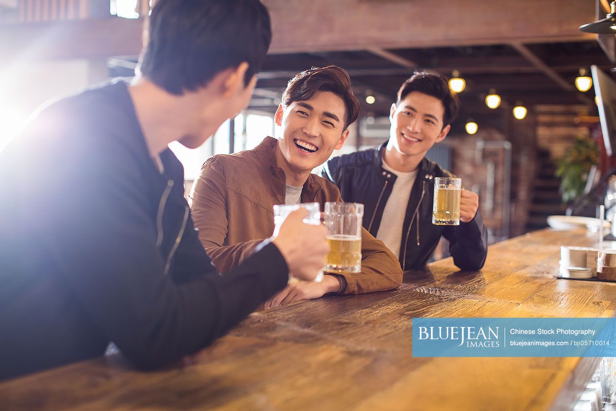 Happy young Chinese men drinking beer in bar