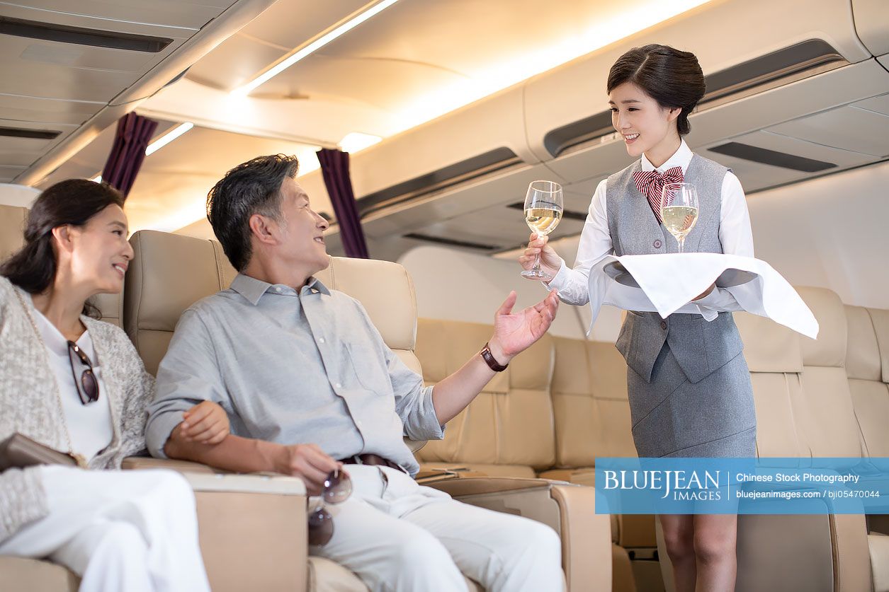 Chinese flight attendant serving wine to mature couple
