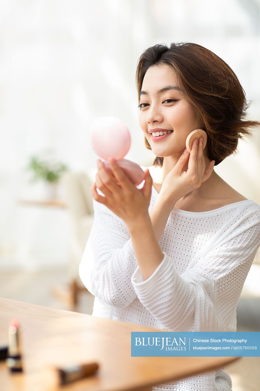 Young Chinese woman applying makeup at home