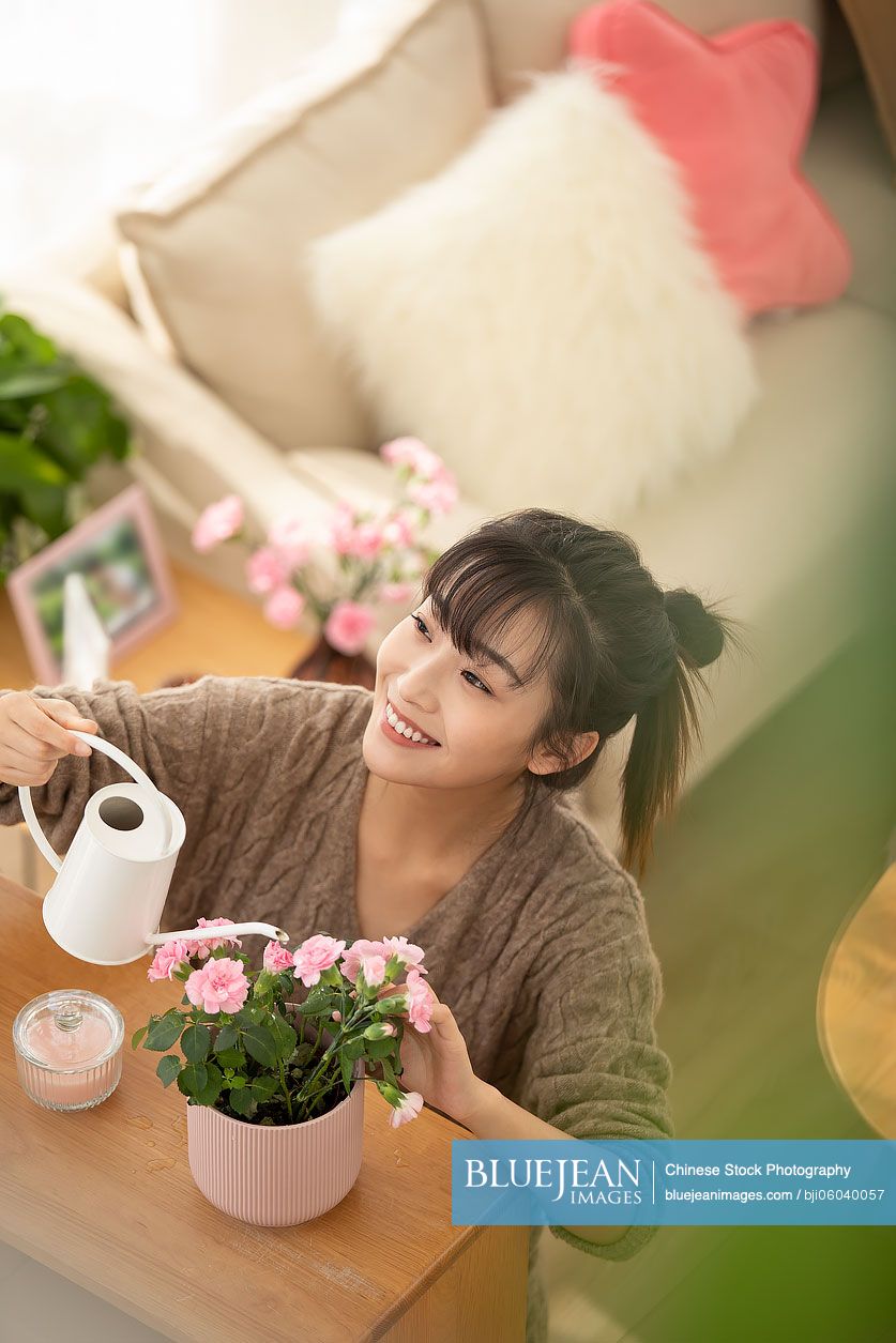 Young Chinese woman watering flowers at home