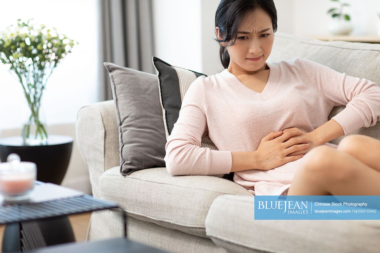 Young Chinese woman having a stomachache on sofa