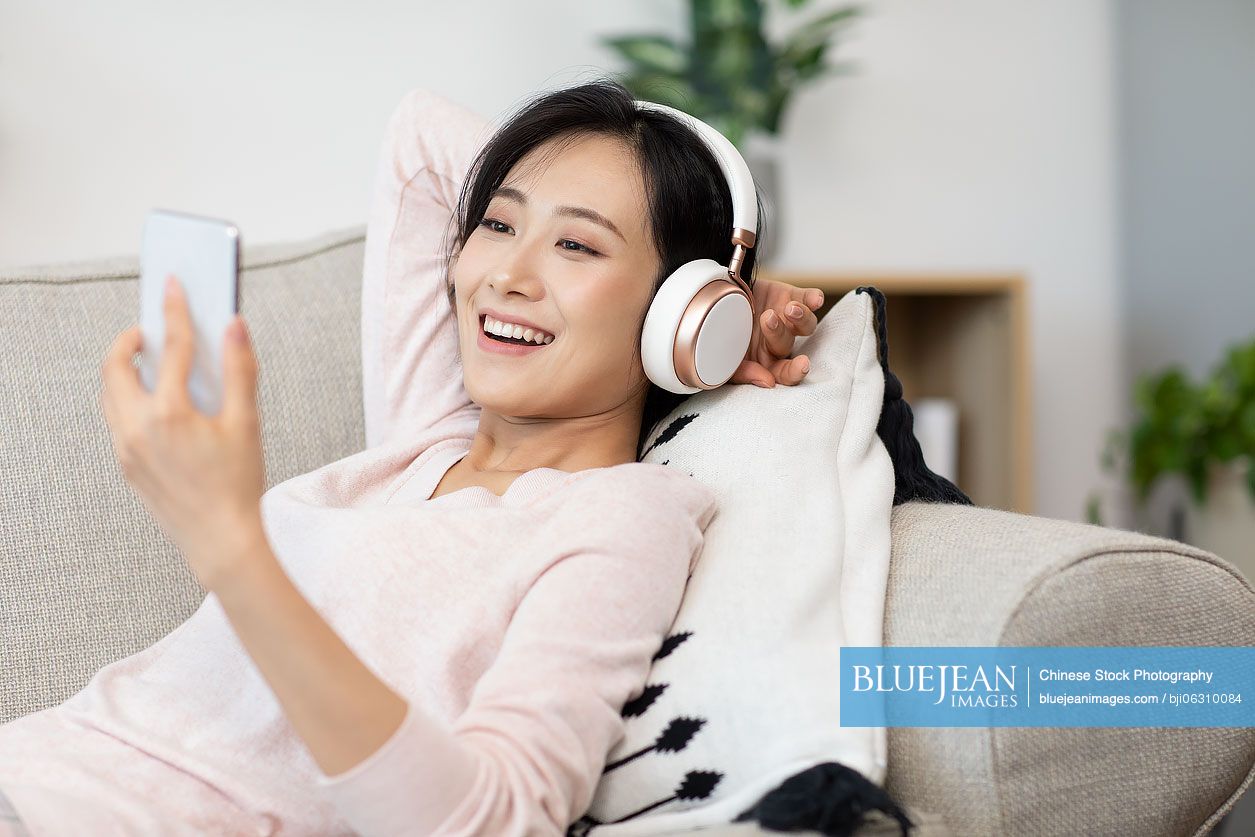 Happy young Chinese woman wearing headphones on sofa