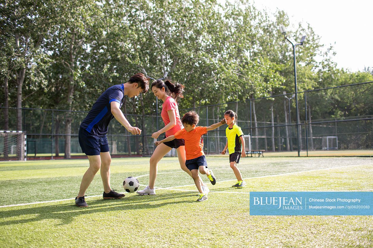 Happy young Chinese family playing football on soccer field