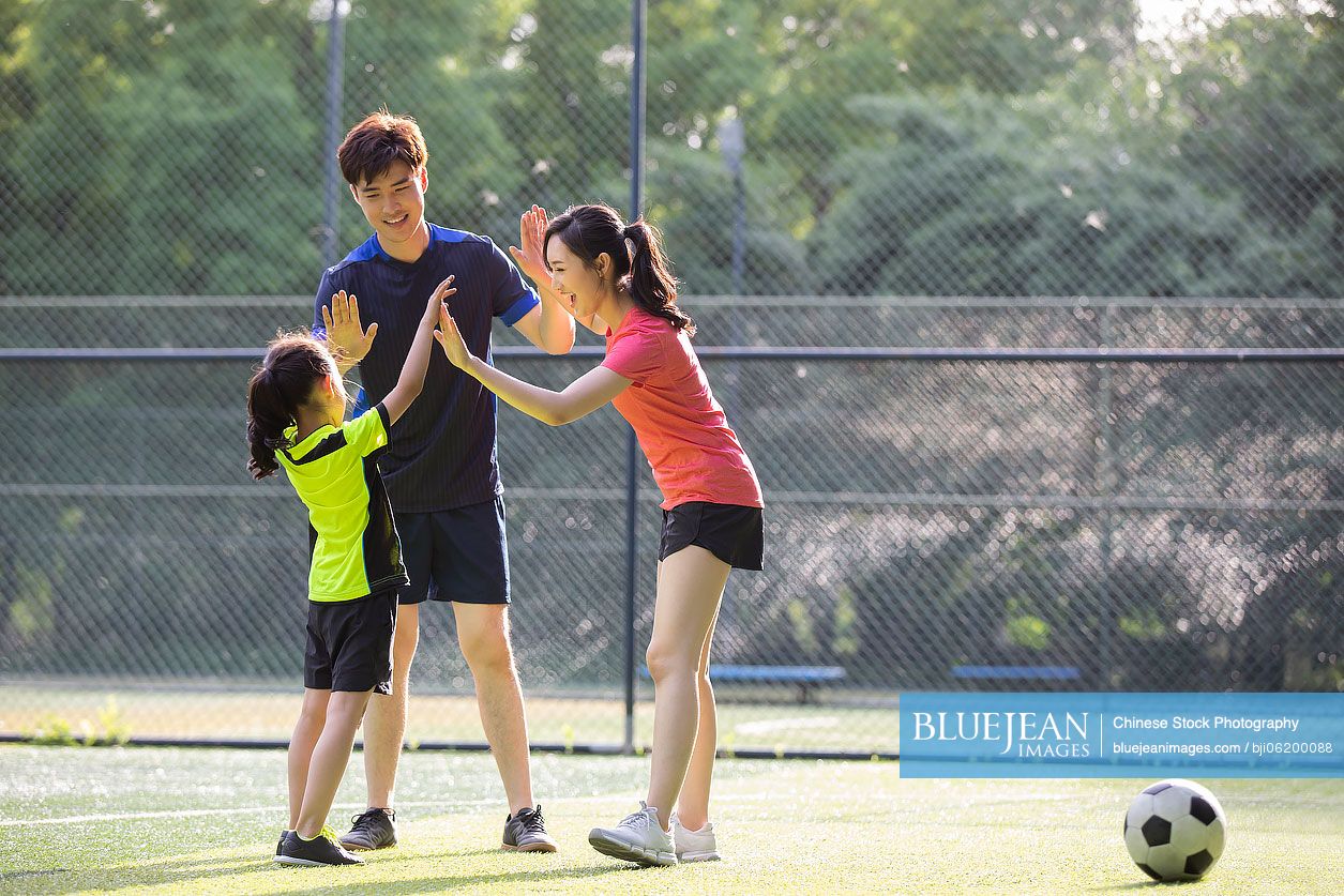 Happy young Chinese family playing football on soccer field