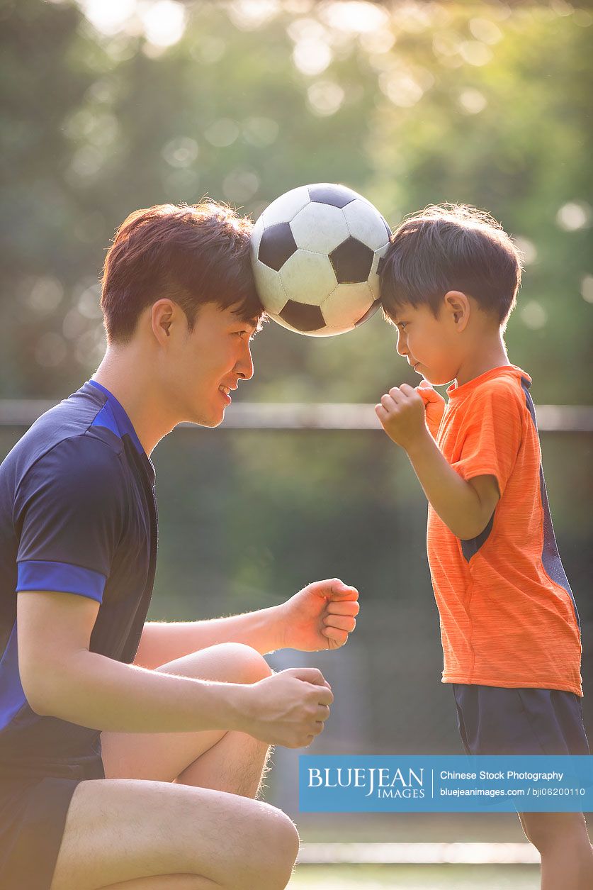 Chinese father and son playing football on field